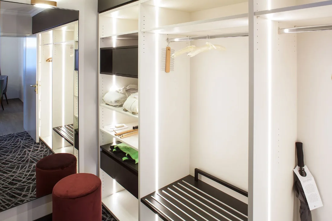 Offene Hotelgarderobe in Weiß mit LED-Lichtlinien, Kofferbank und Spiegel