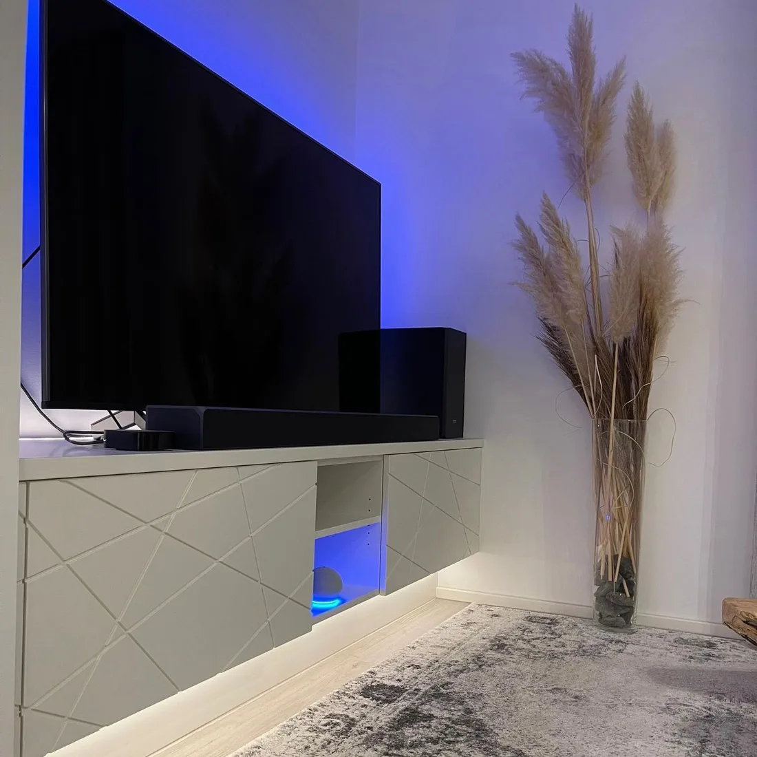 Weißes schwebendes TV-Lowboard mit diagonal gefrästen Fronten und indirekter Beleuchtung