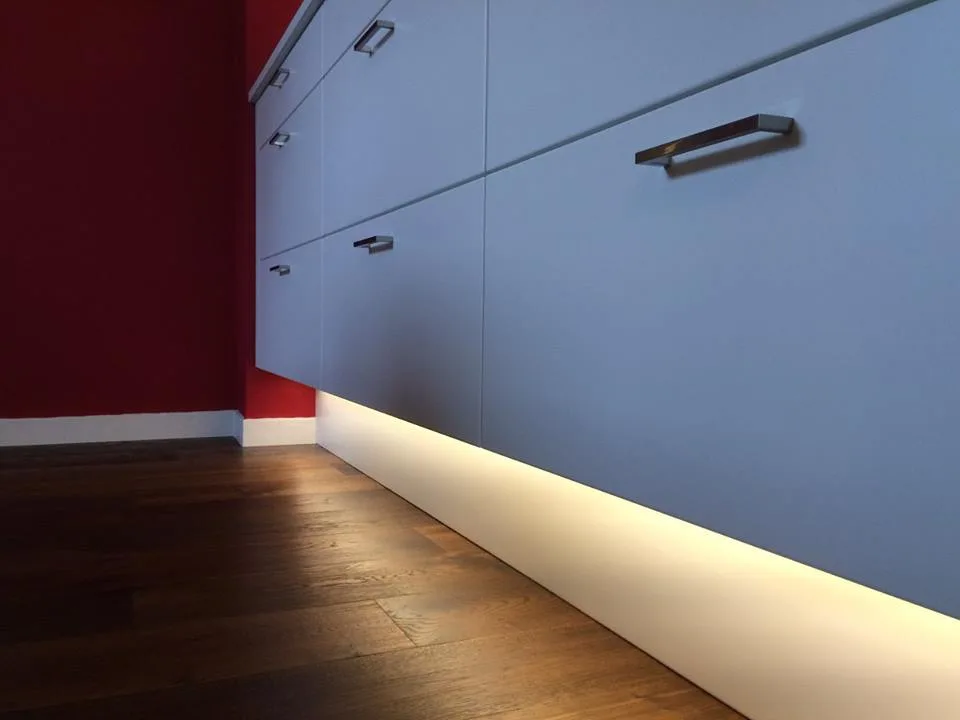 Wandhängendes hellgraues Sideboard mit Stangengriffen und LED-Sockelbeleuchtung vor tiefroter Wand